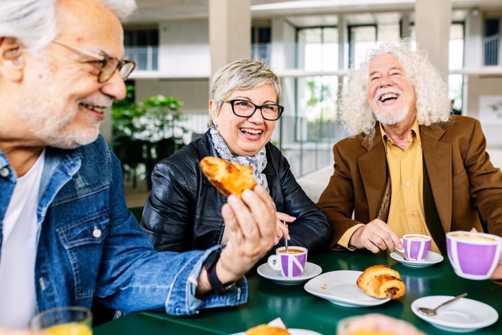 A group of smiling seniors eat croissants and sip on coffee at a restaurant.