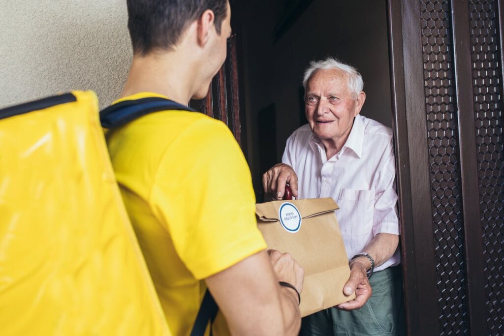 A food delivery service worker delivers a meal to an elderly gentleman.