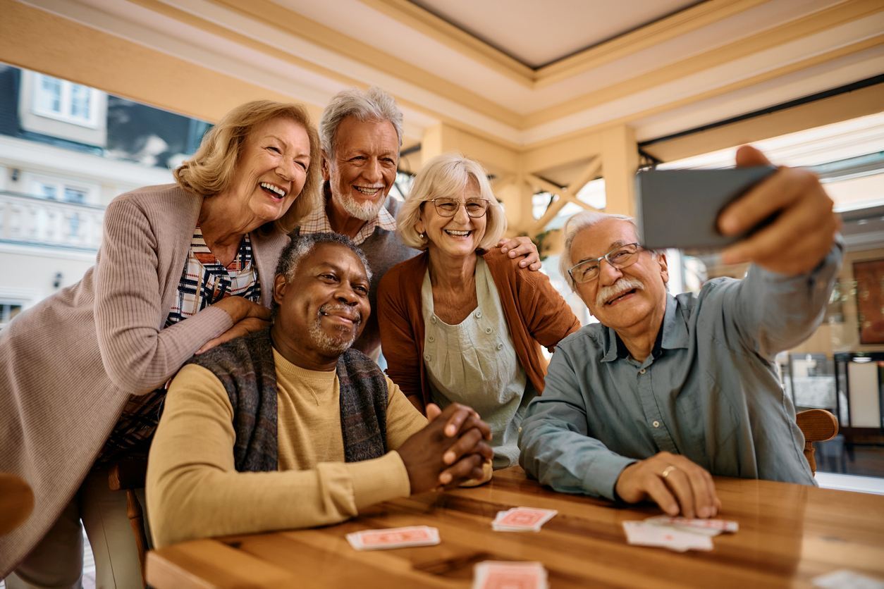 A group of seniors sits around a table playing cards and posing for a picture.