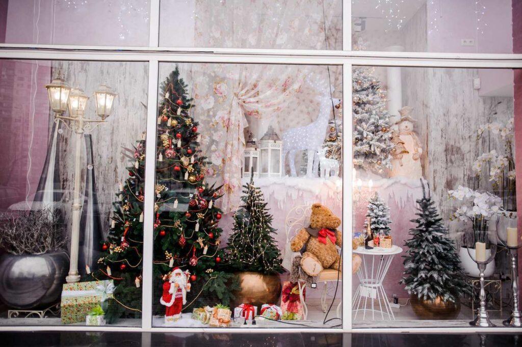 A beautiful festive Christmas windowfront filled with artificial trees, a Santa figurine, miniature lampposts, and toys.